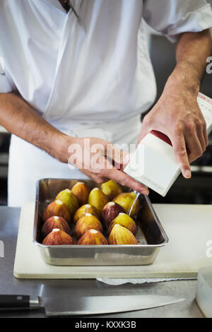 High angle close up of chef travaillant dans la cuisine d'un restaurant de sushi japonais, la préparation de figues dans un plateau métallique. Banque D'Images
