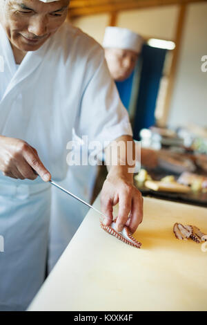 Deux chefs travaillant au comptoir dans un restaurant de sushi japonais, le tranchage tentacule de poulpe. Banque D'Images