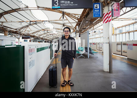 Smiling man avec valise à roulettes sur la plate-forme d'une station de métro, de banlieue de Tokyo. Banque D'Images