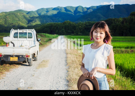 Une jeune femme tenant un chapeau de soleil, debout sur une route par des champs de rizières. Banque D'Images