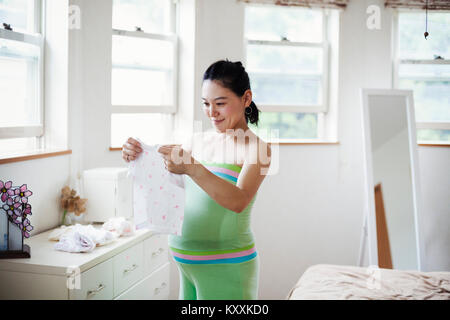 Une femme enceinte dans une pépinière de bébé prix, pliage de vêtements de bébé. Banque D'Images