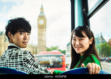 Sourit l'homme et la femme aux cheveux noirs assis à l'avant sur le dessus d'un Double-Decker bus à Londres, looking at camera, chambres du Parlement et Bi Banque D'Images