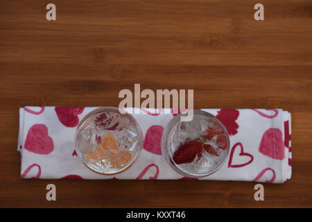 Nourriture et boisson photographie image de cubes de glace dans un verre d'eau gazeuse avec des oranges et des fraises sur blanc rouge amour coeur tissu motif Banque D'Images