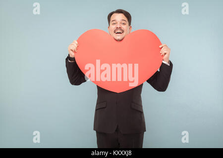 Bien habillé adult man holding big red heart shape et souriant. Studio shot, isolé sur fond bleu clair Banque D'Images