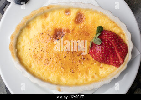 Crème dessert sucré et crémeux faite d'oeufs, le lait et le sucre surmonté d'une fraise en tranches dans une assiette blanche