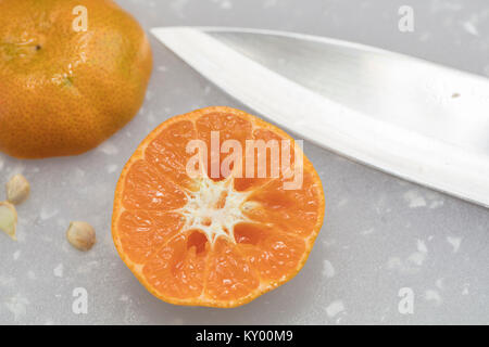 La mandarine en cours de fabrication sur une planche à découper, couteau et graines Banque D'Images