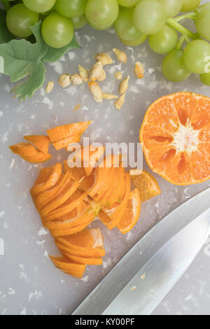 La mandarine étant sur une planche à découper en tranches avec des raisins, des semences et des couteaux Banque D'Images