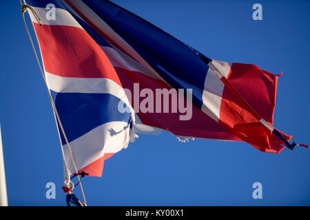 Lambeaux d'un Union Jack flag voltigeant dans le vent contre un ciel bleu. Banque D'Images