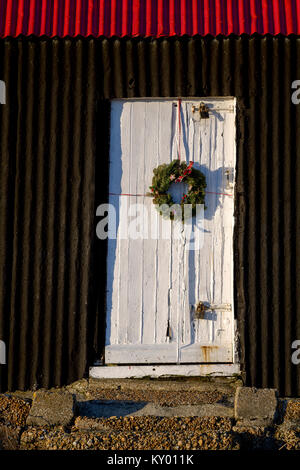 Couronne de Noël est placé sur la porte blanche de la cabane noire et rouge à Rye Harbour. Banque D'Images