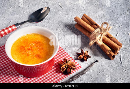 Crème brûlée crème brûlée, (crème brûlée) sur une serviette à carreaux rouge et blanc avec des cuillères, des bâtons de cannelle et anis étoile sur fond de béton gris Banque D'Images