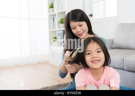 Joli sourire à l'aide de mère aidant pinceau heureux mignon petit fille peigner les cheveux. Banque D'Images