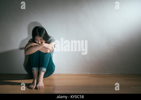 Belle jeune fille ayant abusé de peur de l'expérience et assis sur un plancher en bois se détendre dans mur blanc arrière-plan. Banque D'Images