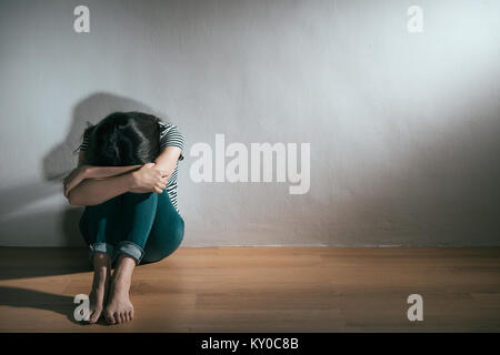 Belle jeune femme ayant la maladie dépression adolescent assis sur le plancher en bois qui crie dans un fond blanc. Banque D'Images