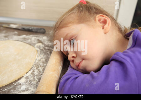 Portrait de l'enfant fatigué dans la cuisine. Petite fille blonde dormir près de la pâte. Banque D'Images