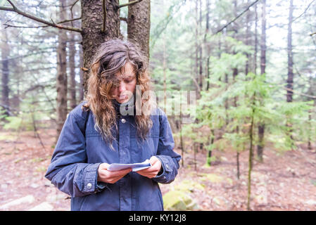 Jeune femme hiker perdu dans une forêt de pins sur l'automne froid jour d'hiver de l'automne avec le blason en regardant les instructions imprimées sur du papier Banque D'Images