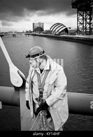 Image noir et blanc vue rapprochée de l'homme avec costume haute visibilité, debout avec une grande grue industrielle sur la rivière Clyde, Glasgow. Banque D'Images