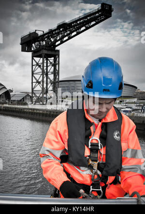 Image en couleur mélangée vue latérale de l'homme vêtue d'un costume haute visibilité, debout avec une grande grue industrielle sur la rivière Clyde, Glasgow. Banque D'Images