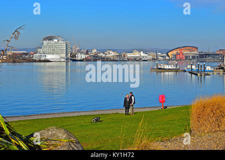 Un couple en train de marcher autour de la baie de Cardiff. avec St David's Hotel,Pierhead bldg (rouge), à l'Assemblée galloise Bldg (Senydd) & Millennium Centre(or) en arrière-plan. Banque D'Images