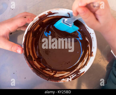 Mains d'un enfant jouer le pâtissier mélanger le chocolat dans un bol avant de le verser dans les moules à chocolat. Vue de dessus. Banque D'Images