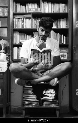 Jeunes adultes en garçon avec les jambes croisées, en position assise, en face de la lévitation d'une étagère, la lecture d'un livre. Banque D'Images