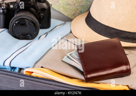 Porte-monnaie avec de l'argent, l'appareil photo et de l'habillement close-up dans suitcase Banque D'Images
