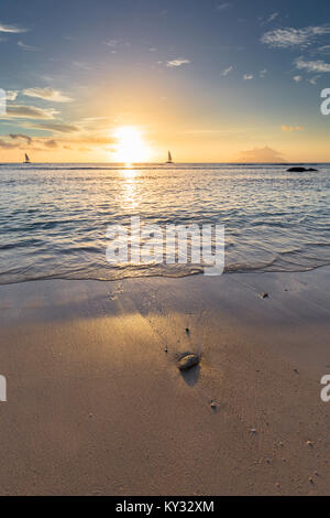 Coucher de soleil sur l'océan avec deux voiliers sur l'horizon et un morceau de corail sur la plage Banque D'Images