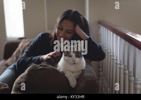 Teenage girl sitting with cat on sofa in living room Banque D'Images