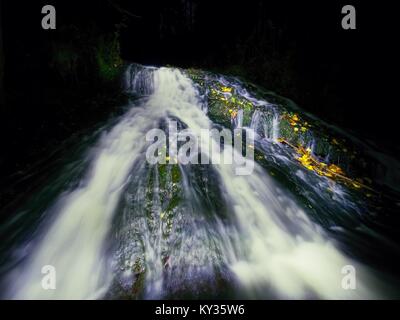 Cascade de nuit. Une pulvérisation d'eau en blanc sur une chute d'eau, l'eau mousseuse est tomber de rock moussues. Le spray créer au niveau de l'eau laiteuse et de gravier Banque D'Images