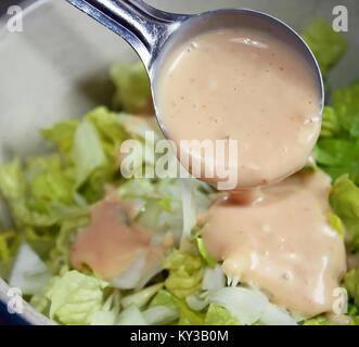 Cuillère à soupe crémeuse de Thousand Island Dressing étant versé sur de la salade fraîche Banque D'Images