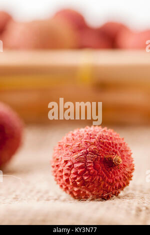 Vue détaillée d'un seul fruit litchi sur un sac en tissu avant de panier brouillée avec d'autres litchis. Banque D'Images