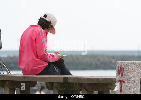 Femelle adulte avec képi siège au banc en bois et lit un livre au parc au bord de mer, de la ville de Hualien, Taiwan Hualien County, Banque D'Images