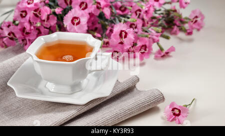Tasse de thé vert sur le tableau blanc avec serviette gris et rose oeillet sauvage Fleurs Banque D'Images