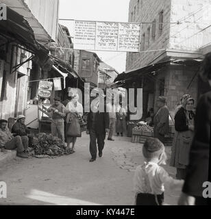 Années 1950, photo historique montrant l'activité dans une rue de Jérusalem, Israël, avec un signe sur la rue écrit en français et de l'herbrew affirmant que les femmes qui passent à travers les rues doivent s'habiller modestement. Banque D'Images