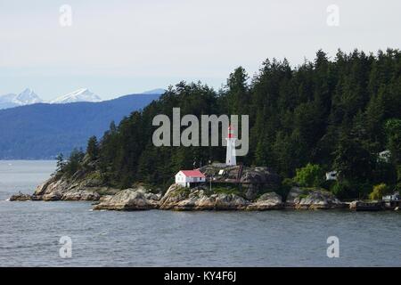 Vue depuis l'eau du phare de Point Atkinson, le Canada avec la forêt verte et enneigés des sommets de montagnes au loin Banque D'Images