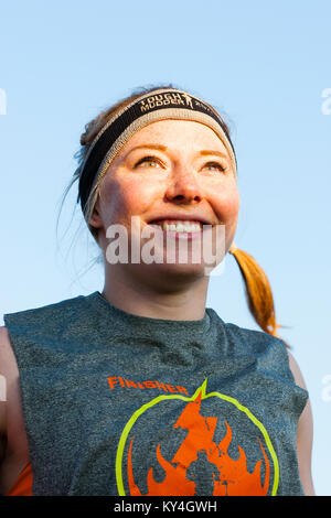 Sussex, UK. Une jeune femme sourit alors qu'elle se réchauffe à l'avance d'un Tough Mudder événement. Banque D'Images