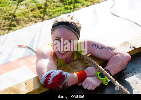 Sussex, UK. Une jeune femme sourit alors qu'elle grimpe sur le haut de l'Everest 2.0 obstacle pendant un événement difficile Mudder. Banque D'Images
