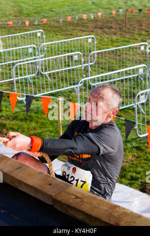 Sussex, UK. Un concurrent masculin grimaces avec effort comme il utilise une corde à grimper l'Everest 2.0 obstacle pendant un événement difficile Mudder. Banque D'Images