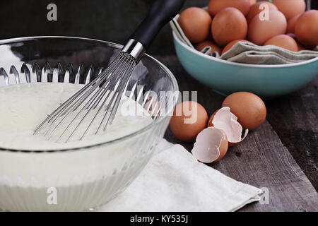 Bol de mélange de la pâte à crêpes faites maison avec des oeufs frais de la ferme brown en arrière-plan. L'extrême profondeur de champ. Parfait pour Mardi Gras. Banque D'Images