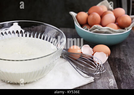 Bol de mélange de la pâte à crêpes faites maison avec des oeufs frais de la ferme brown en arrière-plan. L'extrême profondeur de champ. Parfait pour Mardi Gras. Banque D'Images