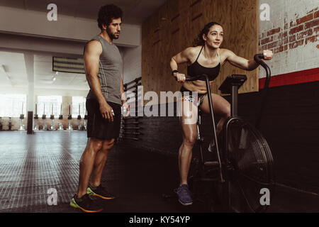 femme de fitness utilisant un vélo pneumatique pour l'entraînement cardio au gymnase avec entraîneur personnel. Femme faisant une séance d'entraînement intense sur vélo de gymnastique avec entraîneur masculin. Banque D'Images