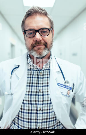 Portrait of mature doctor standing in hospital. Man in lab coat travaillant dans une clinique et à la recherche à l'appareil photo. Banque D'Images