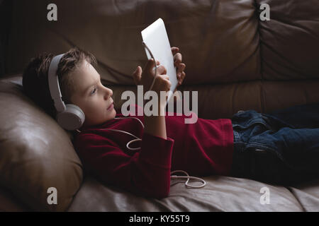 Boy using digital tablet avec des écouteurs dans la salle de séjour
