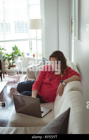 Young pregnant woman sitting on sofa using her laptop Banque D'Images