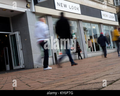 Les gens marcher au-delà d'un nouveau look shop avec une femme appuyée contre une fenêtre à son téléphone Banque D'Images