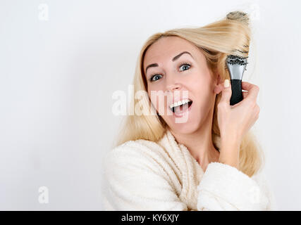 Fille dans un peignoir avec une brosse à pris dans ses cheveux sur fond blanc Banque D'Images