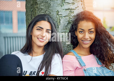 Deux jeunes copines sans souci tout en souriant, assis sur une pelouse, se penchant en arrière sur un tronc d'arbre sur une journée ensoleillée Banque D'Images