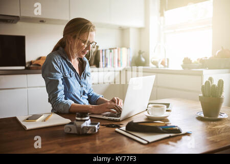 L'accent jeune femme assise à sa table de cuisine à la maison de travailler sur sa petite entreprise avec un ordinateur portable Banque D'Images