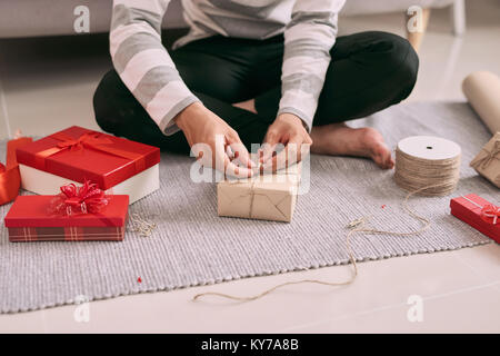 Jeune homme heureux l'emballage cadeau Saint Valentin tout en étant assis sur le plancher Banque D'Images