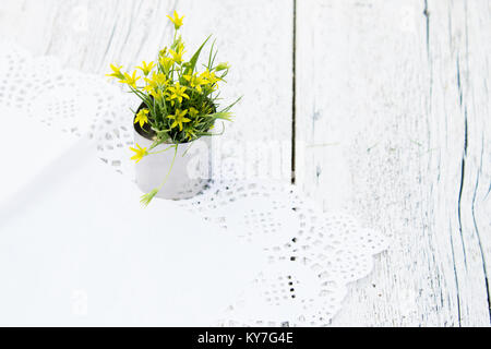 Bouquet de petites fleurs jaunes sur serviette dentelle blanche floue sur fond de bois Banque D'Images