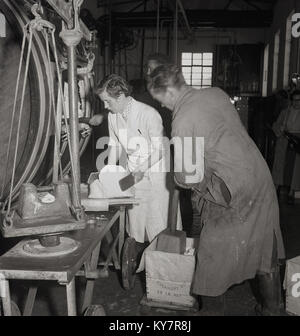 Années 1950, historiques, une femelle dairy travailleur dans un manteau blanc fini de mettre de la baratte à beurre, balances alors qu'un employé de sexe masculin à l'aide d'une presse en bois beurre pousse vers le bas dans une boîte en bois enveloppées, en Irlande. Banque D'Images